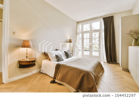 a bedroom with wood flooring and white walls, including a large bed in the room has a brown blanket on it a bedroom with wood flooring and white walls, including a large bed in the room has a brown blanket on it 104452297