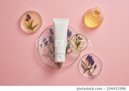 Pastel background for advertising with minimalist concept. An empty plastic tube decorated with fresh lavender and petri dishes containing yellow liquid. Cosmetic mockup with lavender extract. 104452996