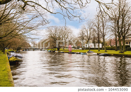 some boats in the water and trees on the other side of the river with no leaves or branches to them 104453090