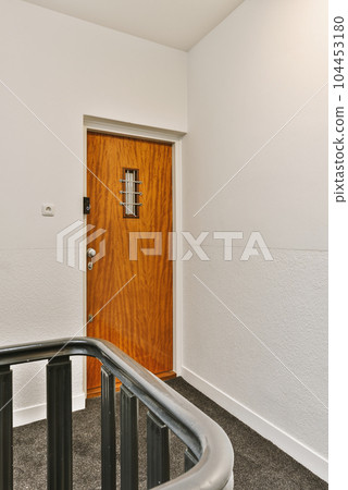 a wooden door in the corner of a white room with grey carpet and black metal handrails on either side a wooden door in the corner of a white room with grey carpet and black metal handrails on either side 104453180