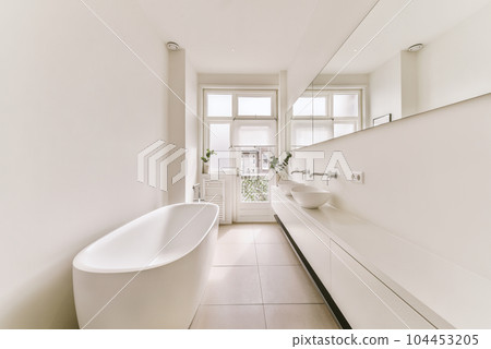 a bathroom with a bathtub and sink in the fore, taken from the side to the other part of the room 104453205