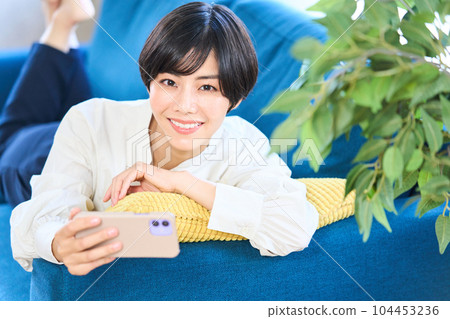 Young woman lying on the sofa, living room, smartphone Young woman lying on the sofa, living room, smartphone 104453236
