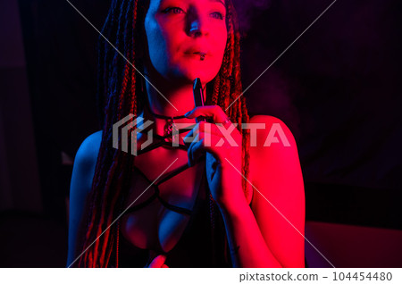 Caucasian girl with dreadlocks smokes a vape in red blue light. Caucasian girl with dreadlocks smokes a vape in red blue light. 104454480