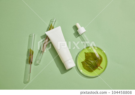 A dropper is leaning on a petri dish, decorated with a tube and two test tube containing beefsteak leaves. Skin care concept of Beefsteak Plant (Perilla frutescens) extract with empty label 104458808