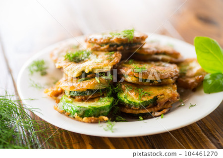 zucchini fried in circles in batter with herbs, in a plate . 104461270