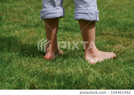 A happy child standing barefoot on the grass, close-up of the feet. Sunny summer day. Summer Vacation A happy child standing barefoot on the grass, close-up of the feet. Sunny summer day. Summer Vacation 104461492