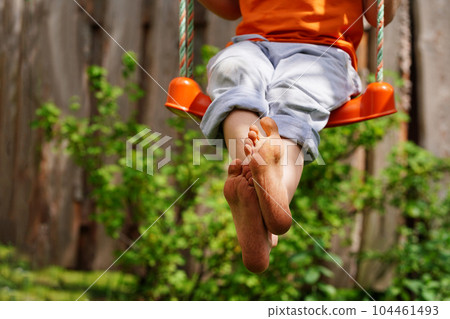 Boy crossed his bare feet. Closeup of feet happy kid sitting and swinging, sunny summer day, countryside background. Child feet barefoot. Boy crossed his bare feet. Closeup of feet happy kid sitting and swinging, sunny summer day, countryside background. Child feet barefoot. 104461493