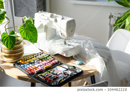 Sewing layout with multicolored spools of thread close-up, needles, electric sewing machine. Filling the thread into the sewing needle, adjusting the tension. hobby, home business 104462228