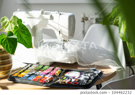 Sewing layout with multicolored spools of thread close-up, needles, electric sewing machine. Filling the thread into the sewing needle, adjusting the tension. hobby, home business Sewing layout with multicolored spools of thread close-up, needles, electric sewing machine. Filling the thread into the sewing needle, adjusting the tension. hobby, home business 104462232