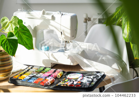 Sewing layout with multicolored spools of thread close-up, needles, electric sewing machine. Filling the thread into the sewing needle, adjusting the tension. hobby, home business 104462233