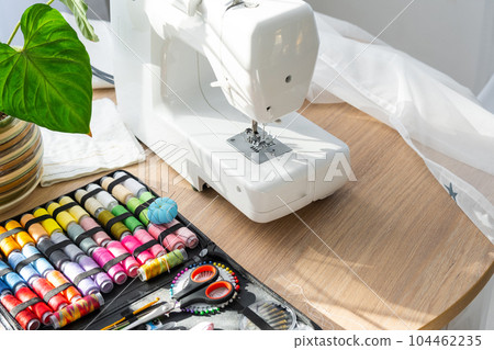 Sewing layout with multicolored spools of thread close-up, needles, electric sewing machine. Filling the thread into the sewing needle, adjusting the tension. hobby, home business 104462235