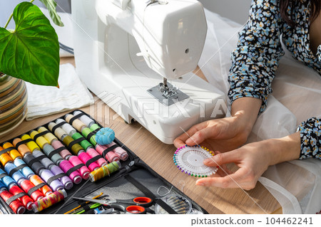 Woman hand close up sews tulle on electric sewing machine. Filling the thread into the sewing needle, adjusting the tension. Comfort in the house, a housewife's hobby, layout of sewing tools Woman hand close up sews tulle on electric sewing machine. Filling the thread into the sewing needle, adjusting the tension. Comfort in the house, a housewife's hobby, layout of sewing tools 104462241