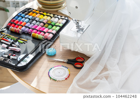 Sewing layout with multicolored spools of thread close-up, needles, electric sewing machine. Filling the thread into the sewing needle, adjusting the tension. hobby, home business Sewing layout with multicolored spools of thread close-up, needles, electric sewing machine. Filling the thread into the sewing needle, adjusting the tension. hobby, home business 104462248