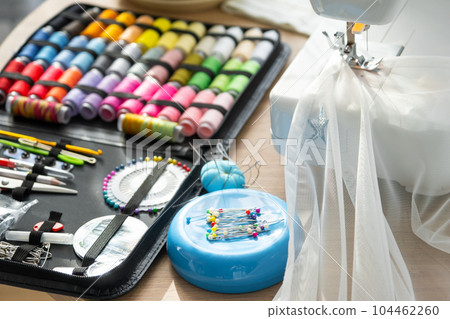 Sewing layout with multicolored spools of thread close-up, needles, electric sewing machine. Filling the thread into the sewing needle, adjusting the tension. hobby, home business Sewing layout with multicolored spools of thread close-up, needles, electric sewing machine. Filling the thread into the sewing needle, adjusting the tension. hobby, home business 104462260