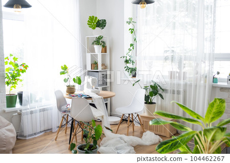 Sewing machine on a round table in the white interior of the house near the window with a transparent curtain, and a home plant in a pot - a modern interior. hobby, home business 104462267