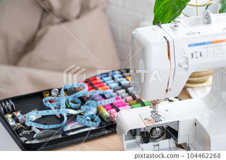 Sewing layout with multicolored spools of thread close-up, needles, electric sewing machine. Filling the thread into the sewing needle, adjusting the tension. hobby, home business 104462268
