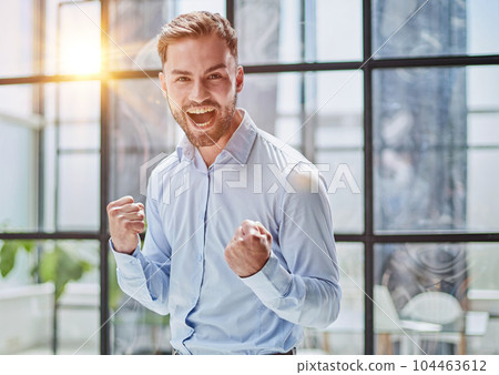 Portrait of a young businessman in a blue shirt shaking his fists celebrating his success 104463612