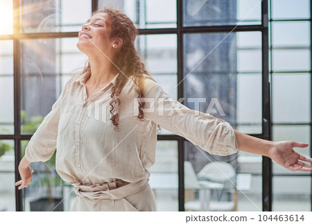 Businesswoman Looking Away While Standing By Window At Office 104463614