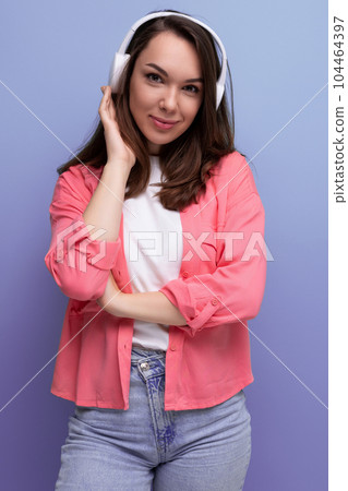 smiling brunette lady with dark hair below her shoulders in a shirt and jeans listens to music in 104464397