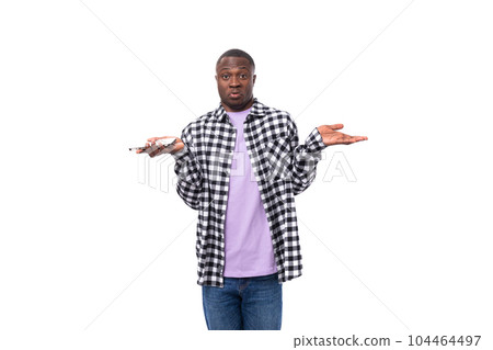 a confused 30 year old african guy dressed in a plaid black and white shirt shrugs his shoulders 104464497