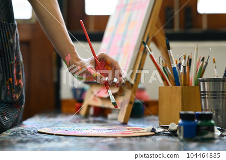 Cropped image of artist standing in front of an easel and dipping brush into color palette 104464885