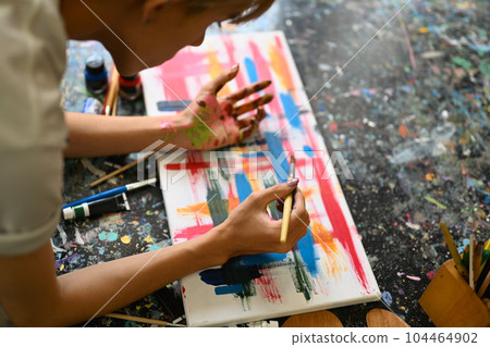 Concentrated man painting picture on canvas with oil paints in bright art studio. Leisure activity and art concept Concentrated man painting picture on canvas with oil paints in bright art studio. Leisure activity and art concept 104464902