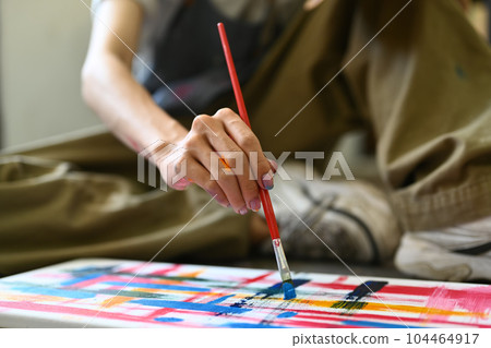 Image of male artist sitting on floor in art studio and painting on canvas with watercolors. Creative hobby and art concept 104464917