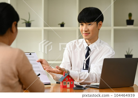 Smiling male realtor holding documents or contract offering to client. Mortgage, real estate and property concept 104464939