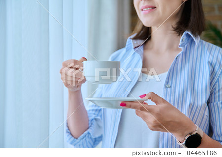 Close-up of a woman's hand with a cup of coffee, window background Close-up of a woman's hand with a cup of coffee, window background 104465186