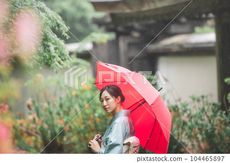 A young woman in Japanese clothes with a red umbrella and a tasteful expression in a landscape full of nature A young woman in Japanese clothes with a red umbrella and a tasteful expression in a landscape full of nature 104465897