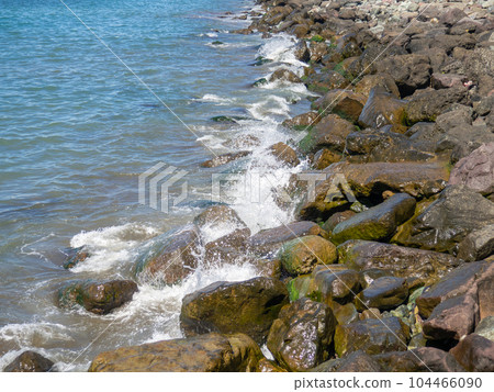 Waves with splashes fall on large stones. Shore view. Beautiful stones that strengthen the shore from the surf. Powerful coastline. Sea foam. The excitement of the sea. 104466090