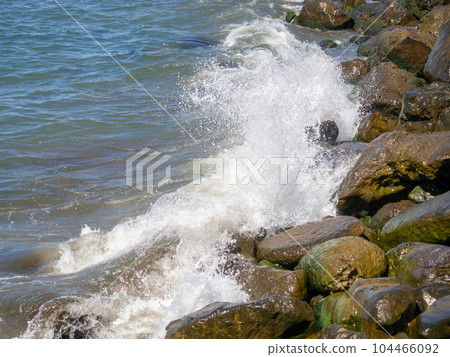 Waves with splashes fall on large stones. Shore view. Beautiful stones that strengthen the shore from the surf. Powerful coastline. Sea foam. The excitement of the sea. Waves with splashes fall on large stones. Shore view. Beautiful stones that strengthen the shore from the surf. Powerful coastline. Sea foam. The excitement of the sea. 104466092