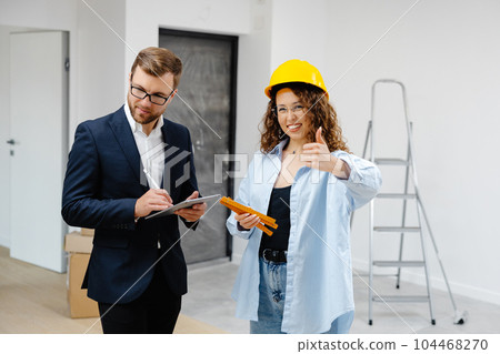 Young designer and customer businessman are designing interior standing with digital tablet in the new living room interior Young designer and customer businessman are designing interior standing with digital tablet in the new living room interior 104468270