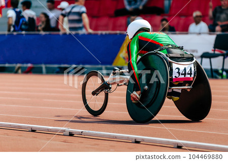 man athlete in wheelchair racing track stadium in para athletics championship, on his head is white helmet 104469880