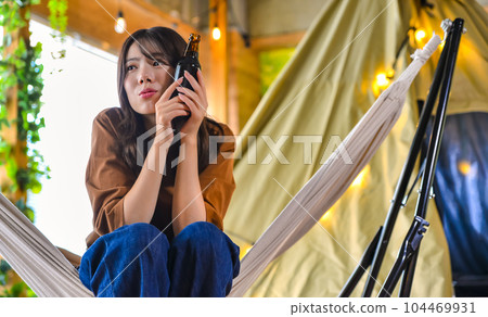 營地吊床上一位年輕女子一手拿著啤酒微笑 104469931