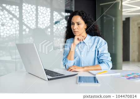 Serious thinking woman working inside office at workplace with laptop, confident hispanic woman looking at technical task, brainstorming solution, business woman with curly hair looking at laptop Serious thinking woman working inside office at workplace with laptop, confident hispanic woman looking at technical task, brainstorming solution, business woman with curly hair looking at laptop 104470814