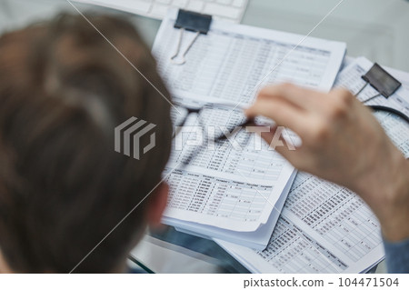 Close-up of a financial businessman holding an information sheet in his hands, reading the company's financial statements for making a financial plan. 104471504