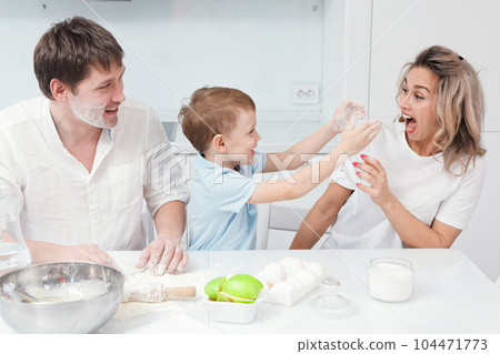 Child and parents are preparing pie from dough in kitchen and got dirty in flour. Young caucasian Child and parents are preparing pie from dough in kitchen and got dirty in flour. Young caucasian 104471773