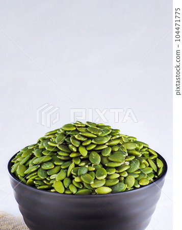 A cup with peeled selected pumpkin seeds on a light background with copy space. Advertising A cup with peeled selected pumpkin seeds on a light background with copy space. Advertising 104471775