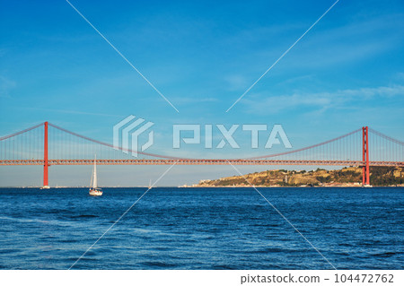View of 25 de Abril Bridge famous tourist landmark over Tagus river and a tourist yacht boat at sunset. Lisbon, Portugal View of 25 de Abril Bridge famous tourist landmark over Tagus river and a tourist yacht boat at sunset. Lisbon, Portugal 104472762