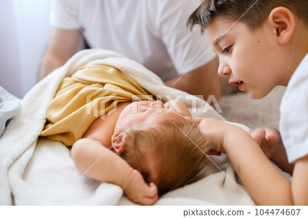 Older brother touches infant newborn in bed 104474607