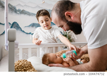Father and brother feed newborn with formula 104474732