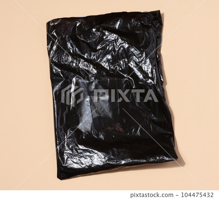 Black plastic bag on a beige background, top view 104475432