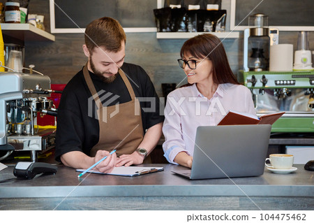 Colleagues male and woman talking, working, using laptop, coffee shop Colleagues male and woman talking, working, using laptop, coffee shop 104475462