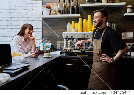 Young male barista talking to woman customer in coffee shop Young male barista talking to woman customer in coffee shop 104475465