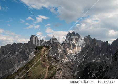 Stunning view of a tourist on the top of a hill enjoying the view of the Cadini di Misurina during sunrise. Cadini di Misurina is a group of mountains located in the Dolomites, Italy. Stunning view of a tourist on the top of a hill enjoying the view of the Cadini di Misurina during sunrise. Cadini di Misurina is a group of mountains located in the Dolomites, Italy. 104478338