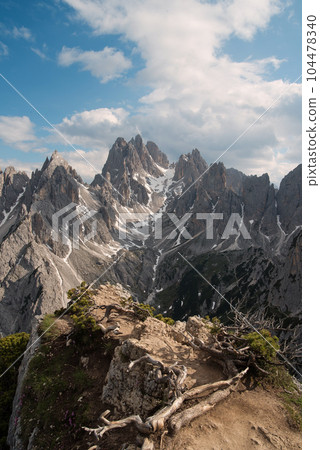 Stunning view of a tourist on the top of a hill enjoying the view of the Cadini di Misurina during sunrise. Cadini di Misurina is a group of mountains located in the Dolomites, Italy. Stunning view of a tourist on the top of a hill enjoying the view of the Cadini di Misurina during sunrise. Cadini di Misurina is a group of mountains located in the Dolomites, Italy. 104478340