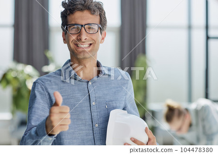 Businessman showing thumbs up - closeup holding a construction hard hat in his hands Businessman showing thumbs up - closeup holding a construction hard hat in his hands 104478380