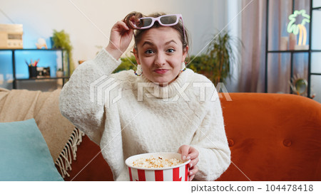 Woman sitting on couch eating popcorn and watching interesting TV 3D film, sport game online at home 104478418