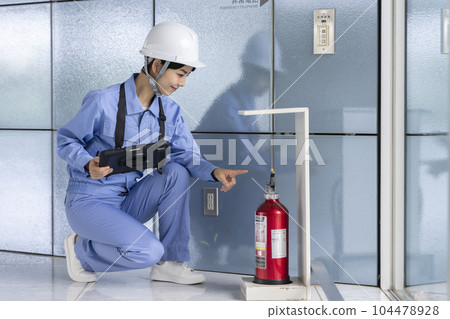 Woman in work clothes inspecting a fire extinguisher Building maintenance image Woman in work clothes inspecting a fire extinguisher Building maintenance image 104478928